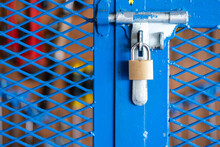 A Key Padlock Is Locking On Metal Fence Gate Knob Of The Hand Tool Storage Box (as Blurred Backgroung). Industrial Object Photo. Close-up And Selective Focus.