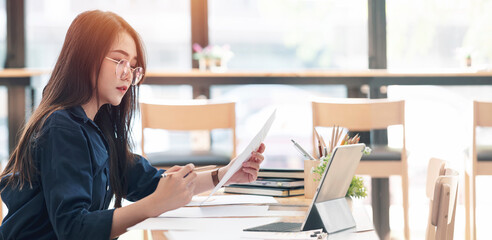 Fototapete - Young female college student using laptop learning online while sitting at co-workspace.