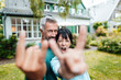 © Westend61 - Cheerful heterosexual couple doing horn sign in backyard