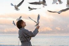 Young Woman Feeding Seagulls At Beach