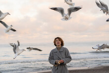 Young Woman Looking At Seagulls Flying At Beach