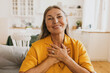 © shurkin_son - Horizontal indoor image of stylish senior woman in yellow jacket doing grateful gesture, putting crossed palms on her chest, being thankful to her children for present, sitting on sofa