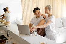 Caucasian Woman Watching Something On Laptop Of Her Asian Boyfriend. Concept Of Relationship And Spending Time Together. Idea Of Domestic Lifestyle. Multiracial Couple In Modern Apartment
