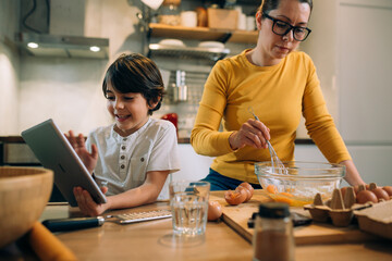 Wall Mural - mother and child in kitchen, preparing cookies. using digital tablet for video chatting