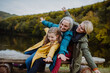Small girl with mother and grandmother sitting on bench and having fun outoors by lake.