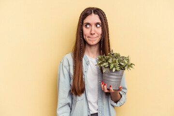 Young caucasian woman holding a plant isolated on yellow background confused, feels doubtful and unsure.