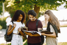 Three International Students Standing In A Park And Holding A Books