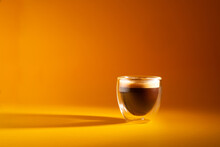 Freshly brewed creamy espresso in a glass coffee cup isolated on yellow background, close up with copy space