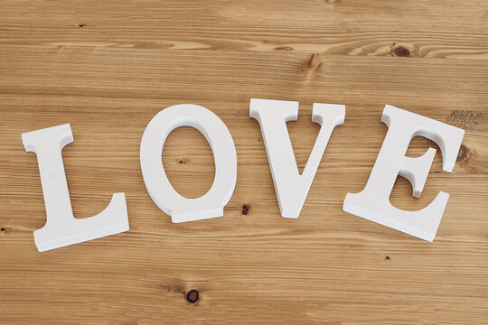 White word Love. Decorative text, letters. Wooden background. Festive banner. Happy Valentine's Day, Mother's Day, March 8, World Women's Day holiday card concept. Wedding decor. Flat lay, top view.