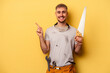 Young electrician caucasian man isolated on yellow background smiling and pointing aside, showing something at blank space.