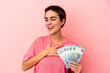 © Asier - Young caucasian woman holding banknotes isolated on pink background laughs out loudly keeping hand on chest.