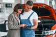 Paying for service. Man repairing woman's automobile indoors