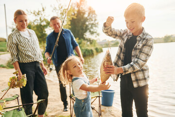 Wall Mural - Big catch. Father and mother with son and daughter on fishing together outdoors at summertime