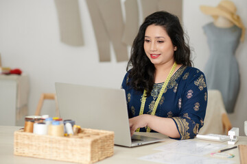 Portrait of happy smiling tailor working on laptop in atelier