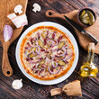 Meat pizza with onions and slices of pork and grated cheese lies on a white plate on a wooden table