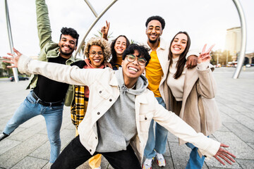 Big group of happy friends stands together on city street with raised arms - Multiracial young people having fun outside - Volunteer with hands up showing teamwork spirit - Community and friendship.