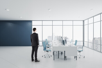 Aufkleber - Businessman standing in modern concrete coworking office room interior with panoramic window with city view, equipment, daylight and furniture.