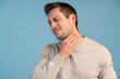 © NFstock - Young caucasian man suffers pain in throat due a virus or infection while standing isolated over blue wall. Stock photo