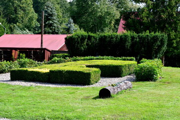 Wall Mural - A view of a well maintained public park with a flower pot shaped like a log, a hedge maze, some shrubbery and a recreational shelter seen on a sunny summer day on a Polish countryside during a hike