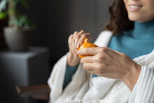Smiling Woman Peels Juicy Ripe Sicilian Tangerine At Home, Selective Focus On Hands. Happy Female Wrapped In White Knitted Plaid Eating Seasonal Winter Fruits, Defocused. High Vitamin C Food Concept
