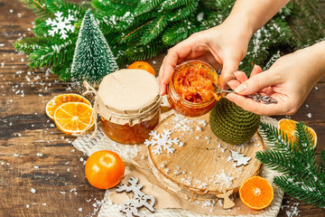 Woman's hands hold orange marmalade or orange jam in a glass jar. Sweet confiture with festive Christmas decor.