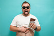Overweight funny man biting large of chocolate with pleased joyful look. Glutton. Excessive sugar intake