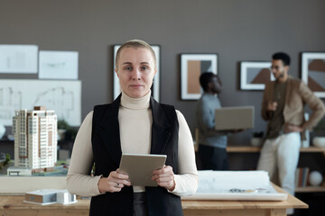 Poster - Contemporary female engineer or architect with digital tablet standing by workplace against two intercultural male colleagues