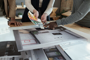 Poster - Hands of three intercultural coworkers standing by workplace with photos of apartment interiors during discussion of color palette