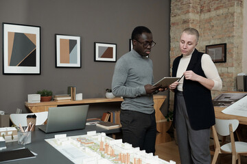 Poster - Young African businessman with tablet making presentation of new architectural project to female colleague at meeting