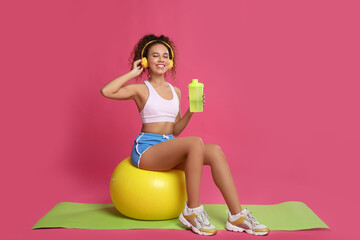 Canvas Print - Beautiful African American woman with headphones  on yoga mat against pink background