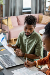 Wall Mural - Young African male economist with financial paper and pen interacting with female colleague by workplace