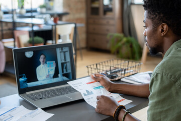 Aufkleber - Young African man watching online video consultation of economist while sitting by table in front of laptop in office