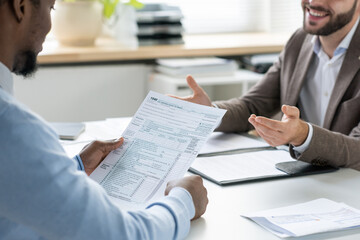 Wall Mural - Hands of young lawyer talking to African male client looking through financial document during consultation