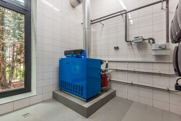 The interior of the boiler room of the house, decorated with white tiles, with a modern water heating system.