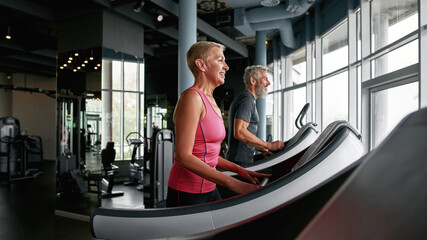 Wall Mural - Active senior couple exercising on treadmills in gym