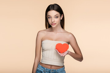 Canvas Print - young woman in crop top with bare shoulders holding red carton heart isolated on beige