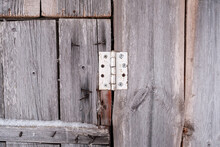 Old Hinge On A Wooden Barn Door With Rusty Nails Sticking Out Of Planks In The Countryside. Abstract Background. 