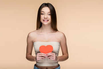 Canvas Print - happy woman in crop top with bare shoulders holding red paper heart isolated on beige