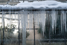 Problem Of Poor Thermal Insulation In Old Orangery Building With Big Icicles Hanging Outside Glass Walls. Early Spring Thaw With Malting Snow On Roof Ripping Water During Day And Frozen At Night