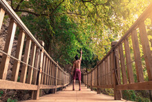 Hombre Joven Latino De Espaldas, Levantando Un Brazo, Parado En Un Puente De Madera En Medio De La Selva