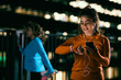 A young night runner using a smart watch app. A young smiling night runner standing outdoors at night, using a smart phone and looking at a smart watch to check on her heart rate.