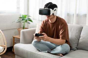 Technology Concept A person wearing a virtual reality headset and holding a black console game while sitting on the sofa