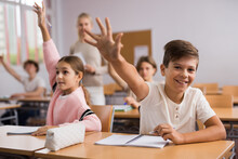 Group Of Happy School Pupils Raise Their Hands Up In Classroom During Lesson In School