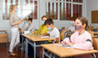 © JackF - School girl in face mask sitting at desk in classroom on background with classmates and teacher