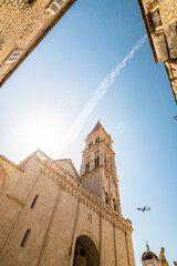 Wall Mural - View of cathedral of St Lawrence, Trogir - Croatia. Down to up look to beautiful ancient church tower. The airplane is landing to Split airport. Aircraft is visible near the tower.