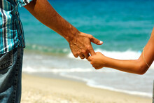 The Parent Holds The Child's Hand On The Beach