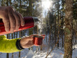 A person pours a hot drink from a steel canteen in the winter forest