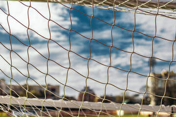 Soccer white net grid on the stadium. Football goal gate, blue sky with clouds on background. View from behind with blurred pitch. Copy space, Healthy lifestyle, sport and recreation concept.