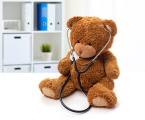 Wall Mural - medicine, healthcare and childhood concept - teddy bear toy with stethoscope over medical office at hospital background
