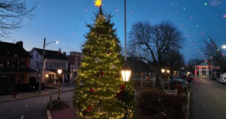 decorated christmas tree at night. lights in town square as snow falls. rising aerial.